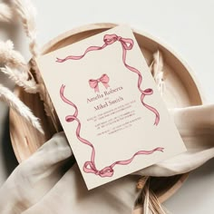 a wedding card on a plate with some feathers in the background and a ribbon tied around it