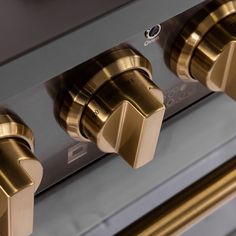 three knobs on the front of a stove top oven with gold handles and brass trim