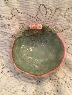 a green bowl sitting on top of a white doily with pink flowers in it