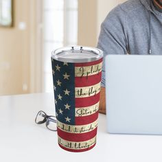 a man sitting in front of a laptop computer with an american flag tumbler next to him