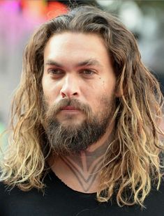 a man with long hair and beard wearing a black t - shirt looking at the camera