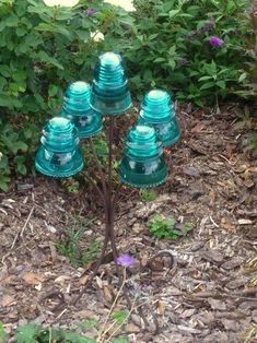 there is a small tree made out of glass bottles in the ground next to flowers