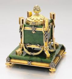 a green and gold plate with a clock on it's stand, sitting on a white surface