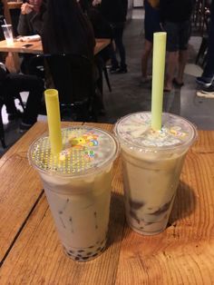 two drinks sitting on top of a wooden table next to each other in plastic cups