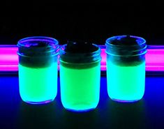 three jars filled with liquid sitting on top of a table next to a neon light