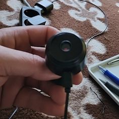 a person is holding a small camera in their hand and some pens are on the floor