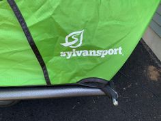 a green bag sitting on the ground next to a metal pole and building with a skyvansport logo on it