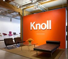 an orange wall with the word knoll on it and two leather chairs in front