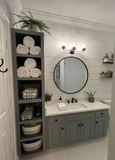 a bathroom with gray cabinets and white towels on the shelves, mirror above the sink