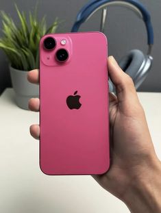 a person holding an iphone in their hand with headphones on the table behind them