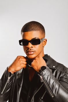 a man in black leather jacket and sunglasses posing for the camera with his hand on his chest