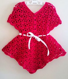 a red crocheted dress hanging on a white wall