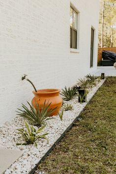 an orange planter sitting on the side of a white brick building next to grass