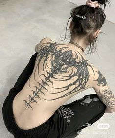 a woman sitting on the ground with her back to the camera and tattoos on her body