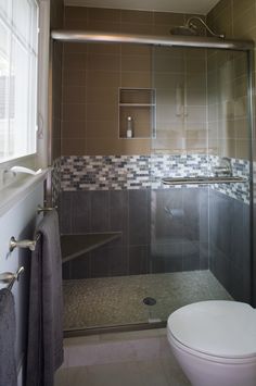 a bathroom with a toilet, shower and tiled walls in grey tones on the wall