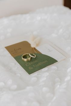 two gold wedding rings sitting on top of a white bed with a price tag attached to the ring