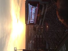 the sun is setting over a stadium full of people and there are signs on the building