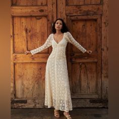 a woman standing in front of a wooden door wearing a white lace dress with long sleeves