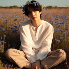 a young man sitting on the ground in a field with blue flowers and wearing a flower crown