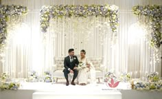 a bride and groom sitting on a stage at their wedding ceremony in front of floral decorations