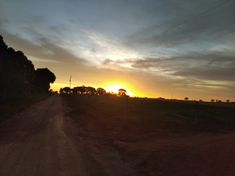 the sun is setting over a dirt road