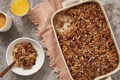 a casserole dish filled with granola next to two bowls of orange juice