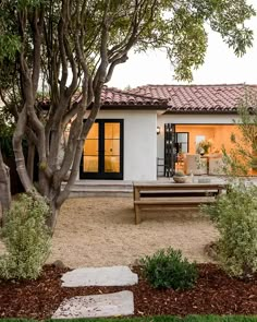 a small white house with a wooden bench in the front yard and trees around it