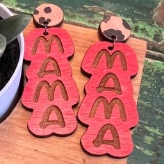 two wooden earrings with letters on them sitting next to a potted succulent