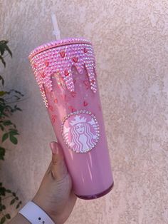 a hand holding a pink starbucks cup with hearts on it