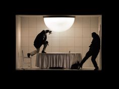 two people jumping in the air near a table with a white cloth on it and a light above them