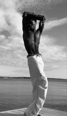 a man standing on top of a wooden pier next to the ocean with his hands behind his head