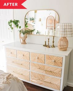 a white dresser with wooden drawers and plants on top, next to a gold mirror