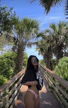 a woman standing on a wooden bridge with palm trees in the background and sunglasses on her head