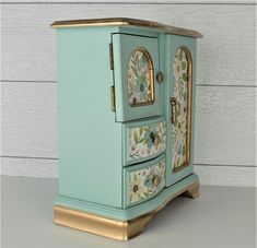 an ornate painted cabinet with gold trimmings and flowers on the front, against a white wall