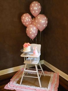 a baby's high chair with pink and white polka dot balloons