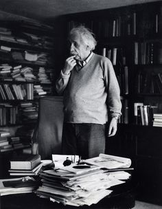 an old black and white photo of a man standing in front of a table full of books