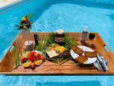 a wooden tray with food on it next to a swimming pool filled with blue water