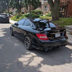 a black mercedes cls parked on the street in front of some trees and houses