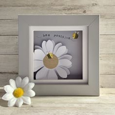 a white flower sitting next to a frame with a bee on it