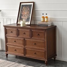 a wooden dresser sitting next to a white wall with a painting on top of it