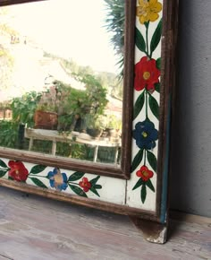 a mirror with flowers painted on it sitting on a wooden floor next to a wall