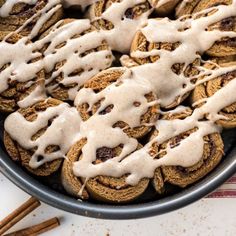 a pan filled with cookies covered in icing next to cinnamon sticks and an orange striped napkin