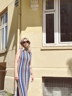 a woman standing in front of a building wearing sunglasses and a colorful dress with stripes on it