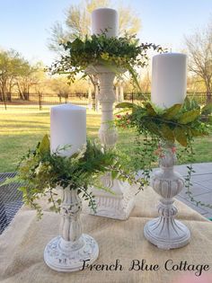 three white candles are sitting on a table with greenery and ivy in the middle