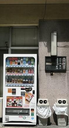 a vending machine sitting on the side of a building next to two trash cans