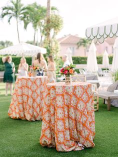 two tables covered with orange and white cloths in the middle of an outdoor area