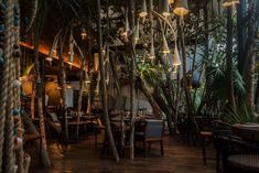 the interior of a tropical restaurant with palm trees and rope hanging from it's ceiling