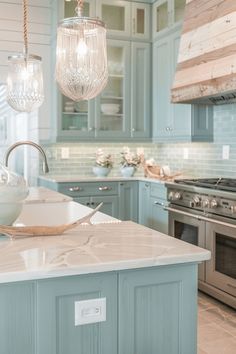 a kitchen with blue cabinets and marble counter tops, two hanging lights above the island