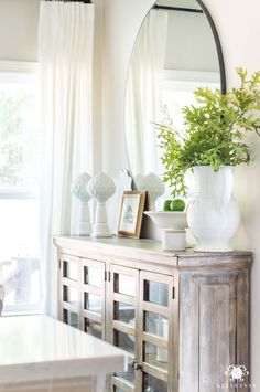 a mirror sitting on top of a wooden cabinet next to a table with vases and plants