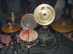 a group of people standing around a drum set with blood on the drumsticks